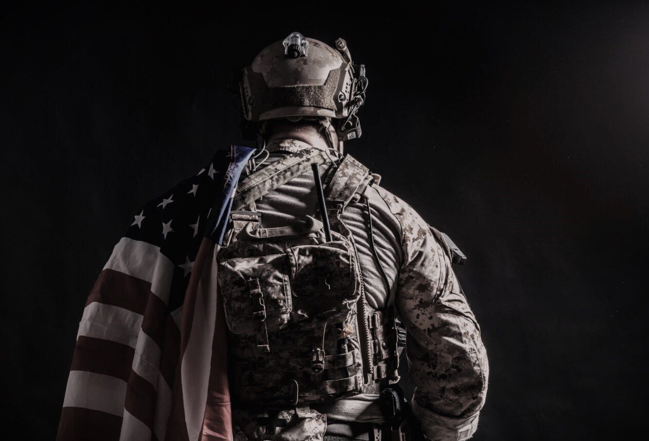 A soldier in camouflage and an american flag.