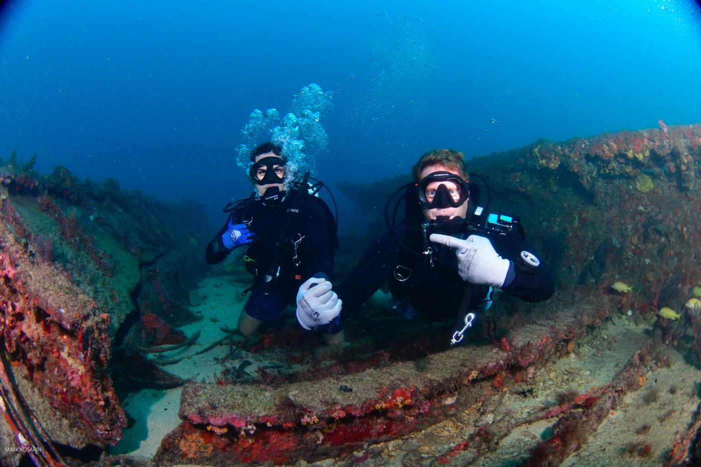 Two scuba divers are sitting on the bottom of a rock.